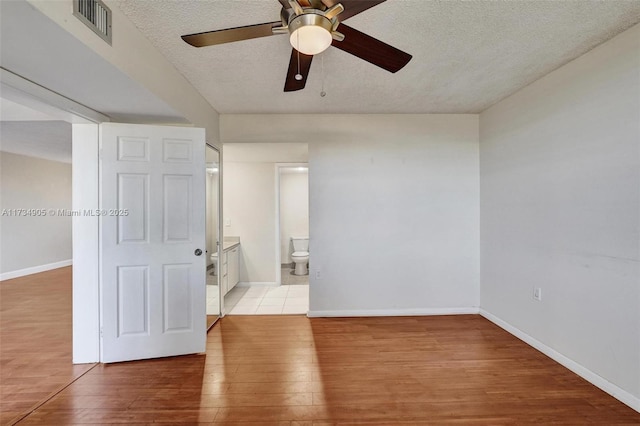 unfurnished bedroom featuring ceiling fan, connected bathroom, a textured ceiling, and light wood-type flooring