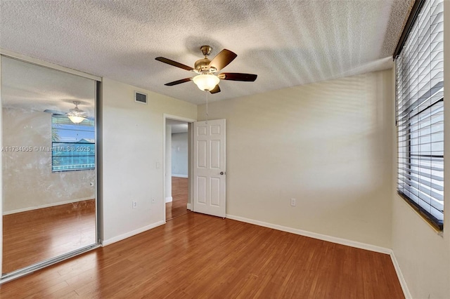 unfurnished bedroom with multiple windows, ceiling fan, hardwood / wood-style floors, and a textured ceiling