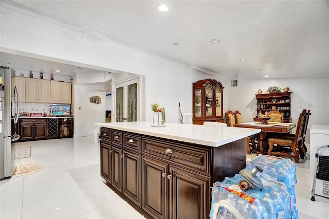 kitchen featuring dark brown cabinets, light tile patterned floors, stainless steel refrigerator, a kitchen island, and cream cabinetry