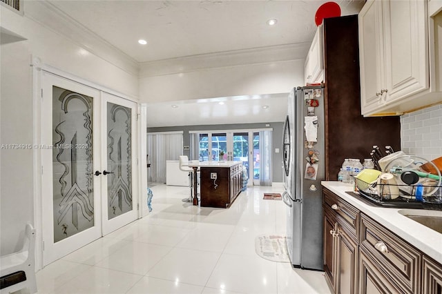 kitchen featuring stainless steel fridge, backsplash, ornamental molding, light tile patterned flooring, and french doors