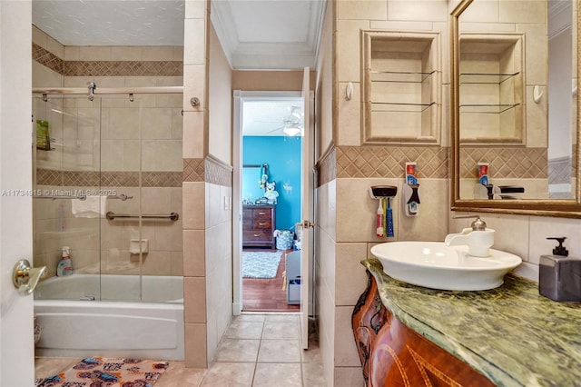 bathroom featuring tile patterned floors, crown molding, bath / shower combo with glass door, tile walls, and vanity