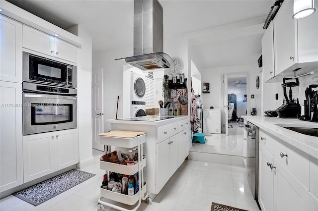 kitchen featuring light tile patterned floors, stainless steel appliances, stacked washer and clothes dryer, island range hood, and white cabinets