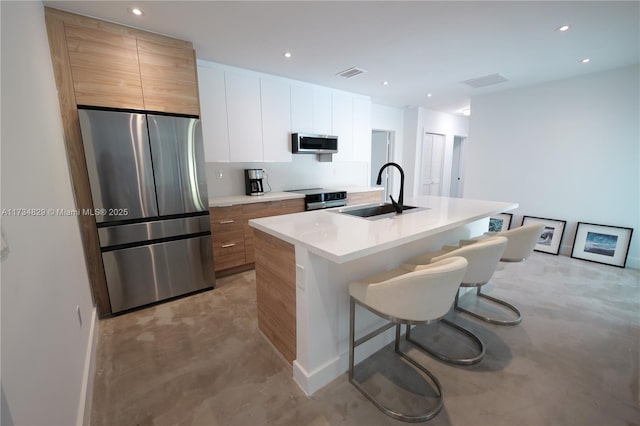 kitchen featuring appliances with stainless steel finishes, sink, white cabinets, a kitchen bar, and a kitchen island with sink