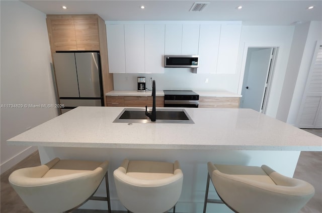 kitchen with white cabinetry, appliances with stainless steel finishes, a kitchen island with sink, and sink