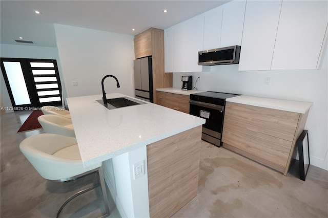 kitchen featuring sink, white cabinetry, a kitchen island with sink, stainless steel appliances, and light stone counters