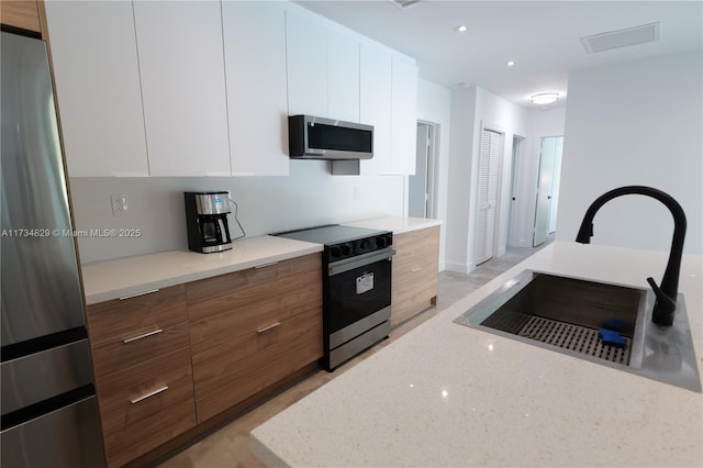 kitchen with white cabinetry, sink, stainless steel appliances, and light stone countertops