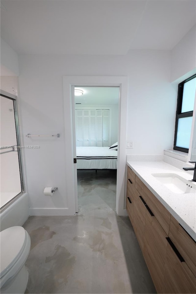 full bathroom featuring concrete flooring, bath / shower combo with glass door, vanity, and toilet