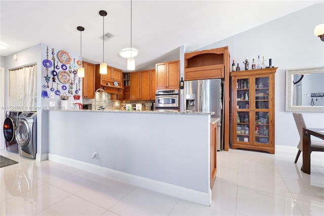 kitchen featuring appliances with stainless steel finishes, decorative light fixtures, light stone counters, kitchen peninsula, and washer and clothes dryer