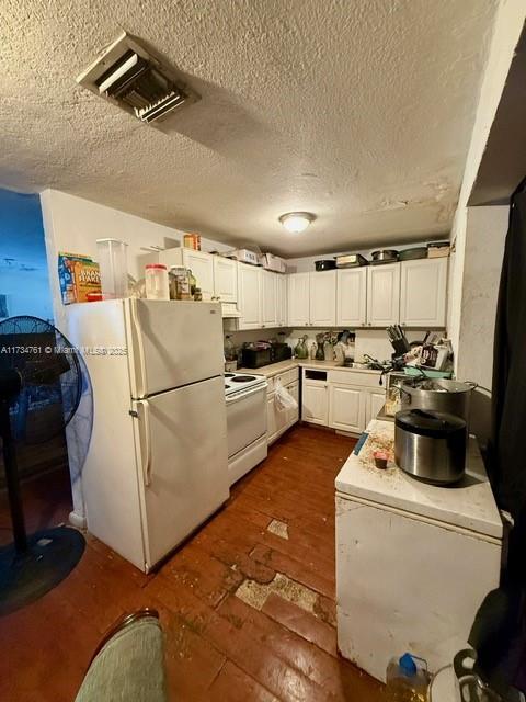 kitchen featuring white appliances, a textured ceiling, dark hardwood / wood-style floors, and white cabinets