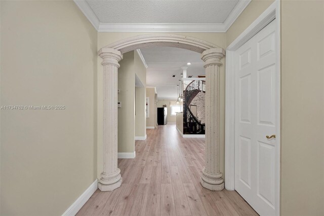 hallway featuring crown molding, light wood-type flooring, a textured ceiling, and ornate columns