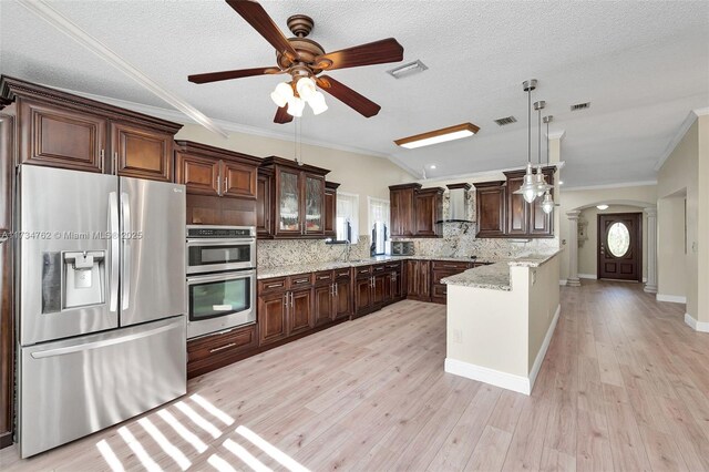 kitchen with appliances with stainless steel finishes, pendant lighting, light stone countertops, wall chimney range hood, and light wood-type flooring