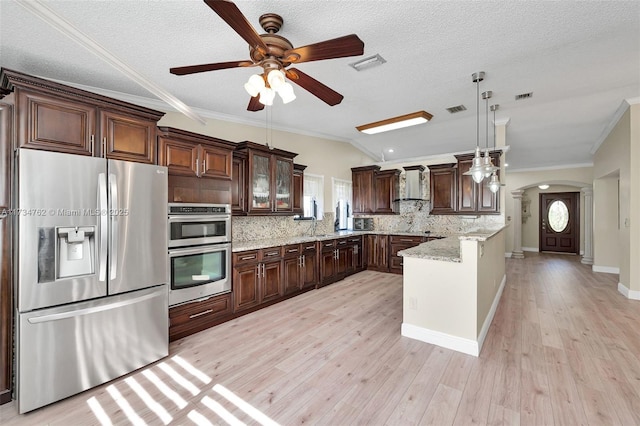 kitchen featuring appliances with stainless steel finishes, light stone countertops, light hardwood / wood-style floors, decorative light fixtures, and wall chimney exhaust hood