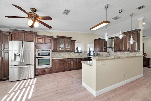 kitchen with dark brown cabinetry, wall chimney range hood, hanging light fixtures, and appliances with stainless steel finishes