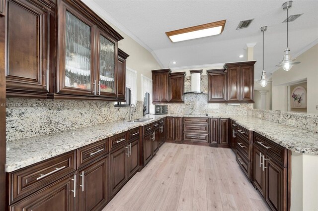 kitchen with crown molding, wall chimney range hood, decorative light fixtures, and sink