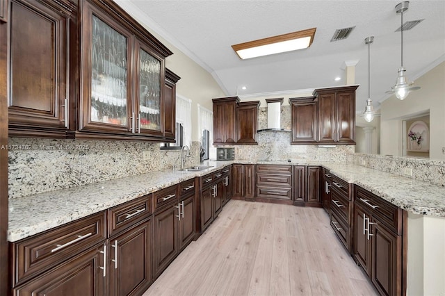 kitchen featuring crown molding, sink, hanging light fixtures, and wall chimney range hood