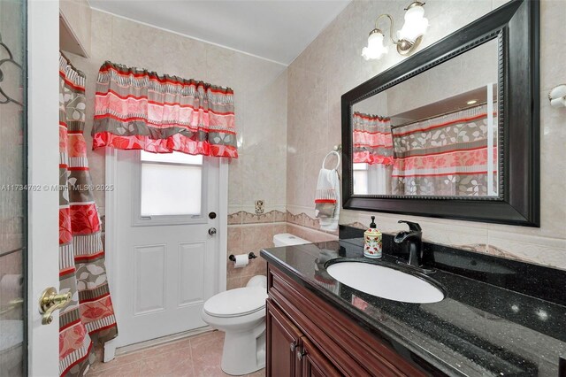 bathroom with curtained shower, tile walls, tile patterned flooring, vanity, and toilet