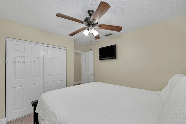 bedroom featuring ceiling fan, light hardwood / wood-style floors, a closet, and a textured ceiling