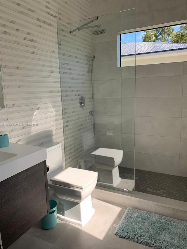 bathroom with tile walls, tile patterned flooring, vanity, a tile shower, and toilet