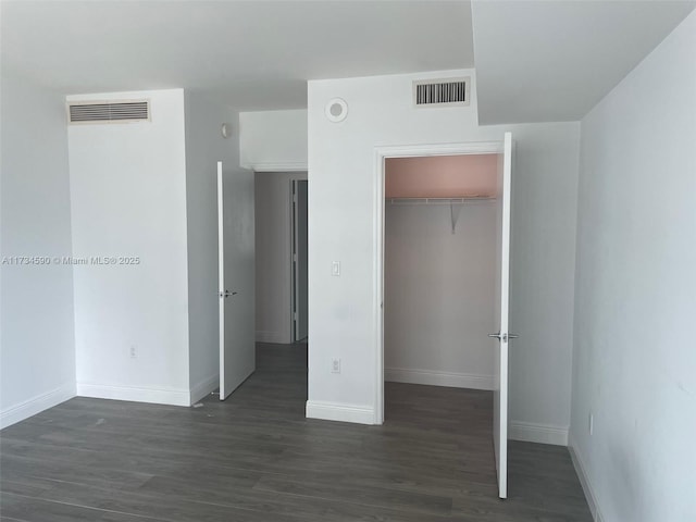 unfurnished bedroom featuring dark wood-type flooring, a walk in closet, and a closet