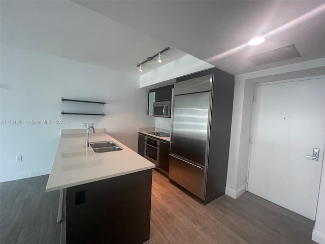 kitchen featuring dark wood-type flooring, rail lighting, sink, appliances with stainless steel finishes, and kitchen peninsula