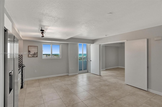 empty room featuring a water view, light tile patterned floors, and a textured ceiling