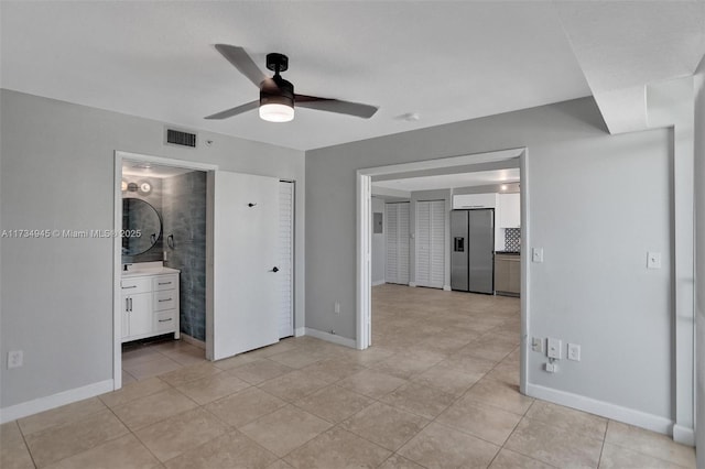 unfurnished bedroom with light tile patterned flooring, ceiling fan, stainless steel fridge, and ensuite bath