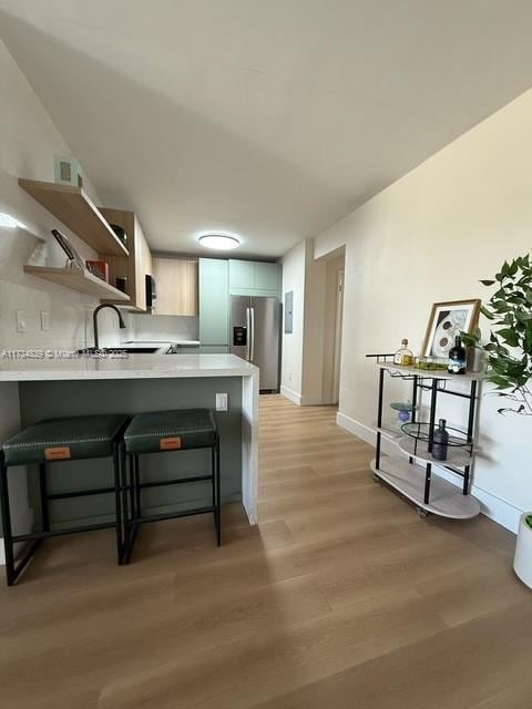 kitchen with sink, a breakfast bar area, stainless steel refrigerator with ice dispenser, kitchen peninsula, and light wood-type flooring