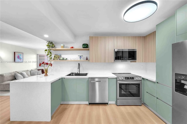 kitchen featuring light wood finished floors, appliances with stainless steel finishes, backsplash, and a sink