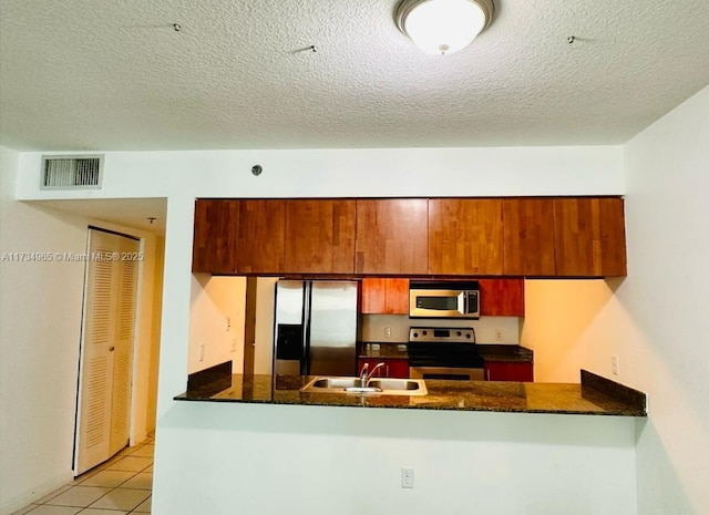 kitchen featuring appliances with stainless steel finishes, sink, dark stone countertops, light tile patterned floors, and kitchen peninsula