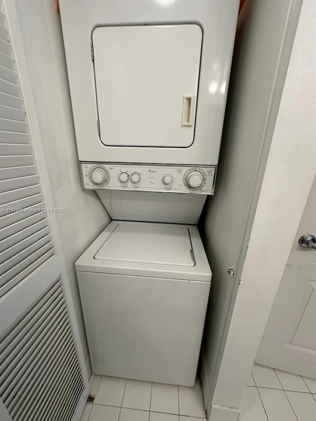 laundry area with stacked washer / drying machine and light tile patterned floors