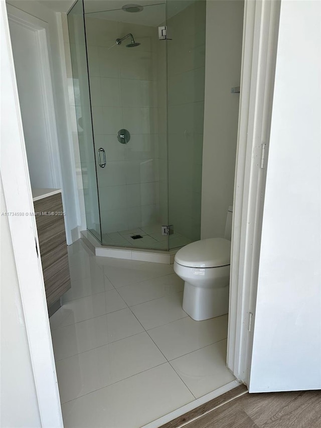 bathroom with tile patterned flooring, a shower with shower door, and toilet