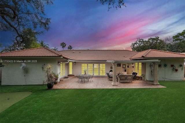 back house at dusk featuring a yard, a patio area, and french doors