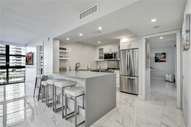 kitchen with white cabinetry, a breakfast bar area, backsplash, kitchen peninsula, and stainless steel appliances