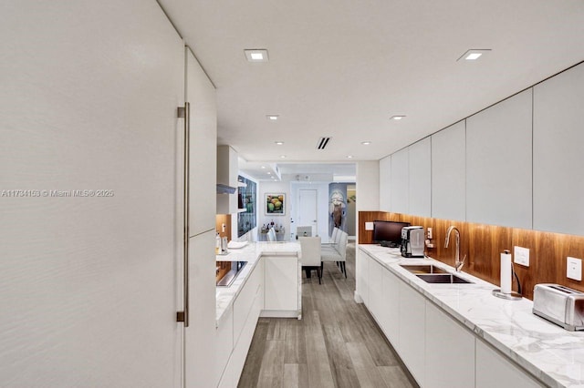 kitchen featuring light stone counters, black electric cooktop, sink, and white cabinets