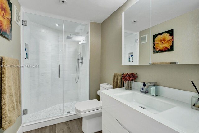 bathroom featuring vanity, wood-type flooring, a shower with door, and toilet