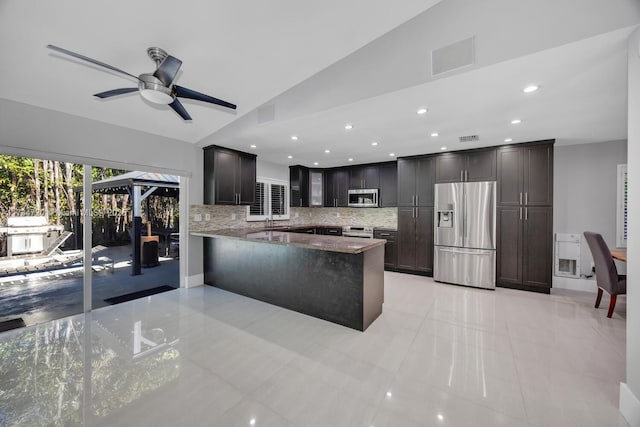 kitchen with lofted ceiling, stainless steel appliances, dark brown cabinetry, decorative backsplash, and kitchen peninsula