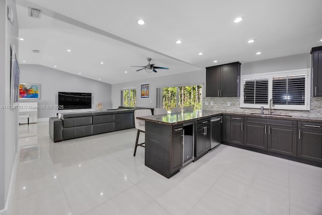 kitchen featuring lofted ceiling, sink, a breakfast bar area, kitchen peninsula, and dark stone counters