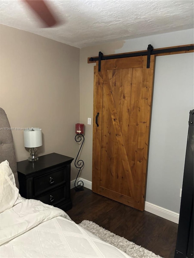 bedroom featuring dark wood-type flooring, a barn door, and a textured ceiling