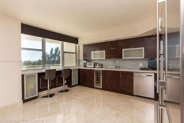 kitchen featuring sink, tasteful backsplash, dark brown cabinets, stainless steel dishwasher, and beverage cooler