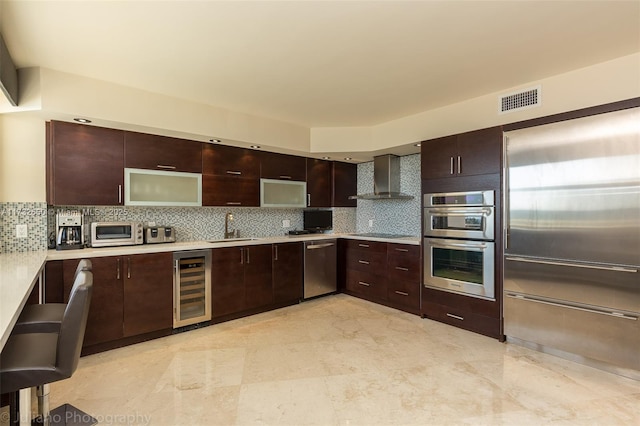 kitchen with appliances with stainless steel finishes, tasteful backsplash, sink, beverage cooler, and wall chimney range hood