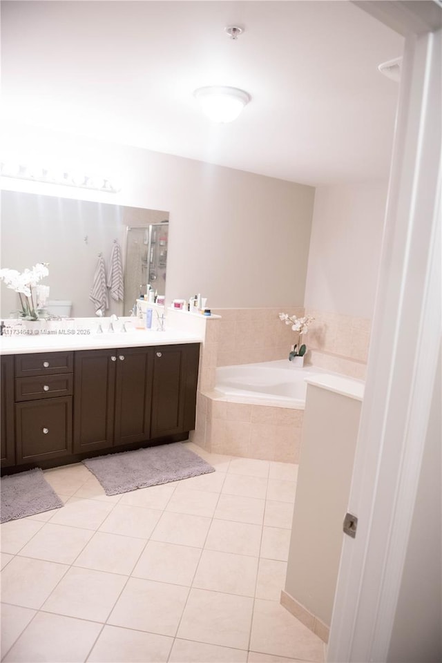 bathroom with a relaxing tiled tub, vanity, toilet, and tile patterned flooring