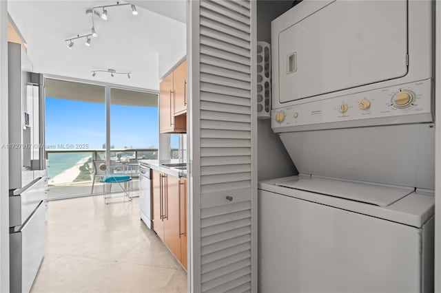 clothes washing area featuring stacked washing maching and dryer, a water view, and track lighting