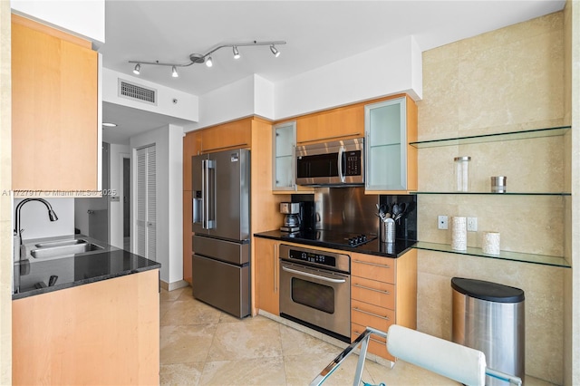 kitchen with rail lighting, sink, appliances with stainless steel finishes, dark stone counters, and decorative backsplash