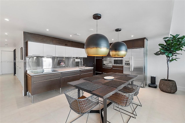 kitchen featuring appliances with stainless steel finishes, white cabinetry, hanging light fixtures, dark brown cabinetry, and decorative backsplash