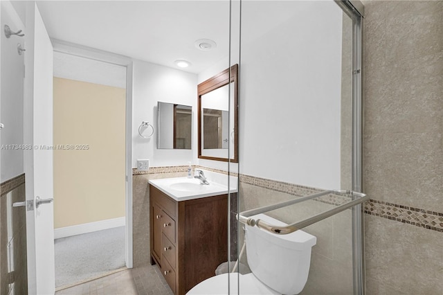 bathroom featuring walk in shower, vanity, toilet, and tile walls