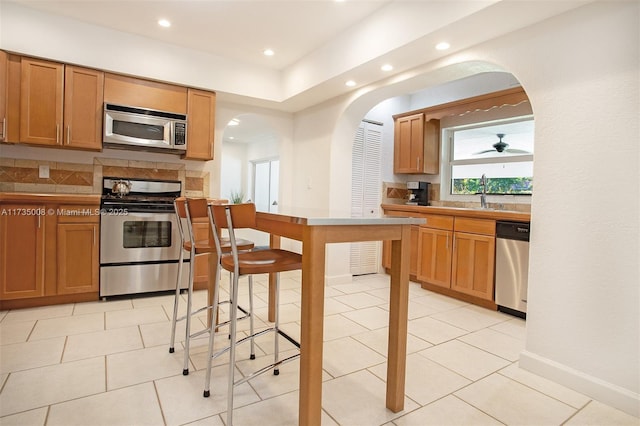 kitchen with light tile patterned flooring, appliances with stainless steel finishes, sink, backsplash, and ceiling fan