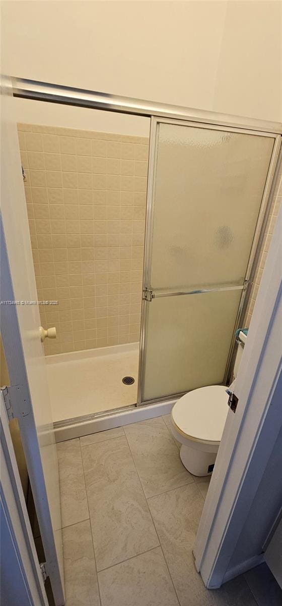 full bath featuring tile patterned flooring, a shower stall, and toilet