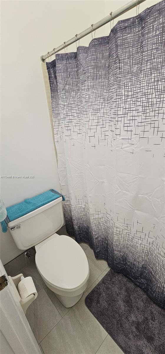 full bathroom with toilet, curtained shower, and tile patterned floors