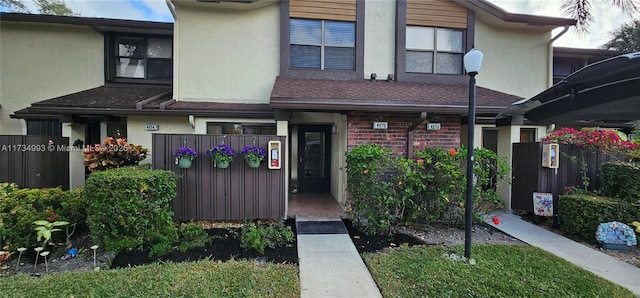 multi unit property featuring roof with shingles, brick siding, fence, and stucco siding