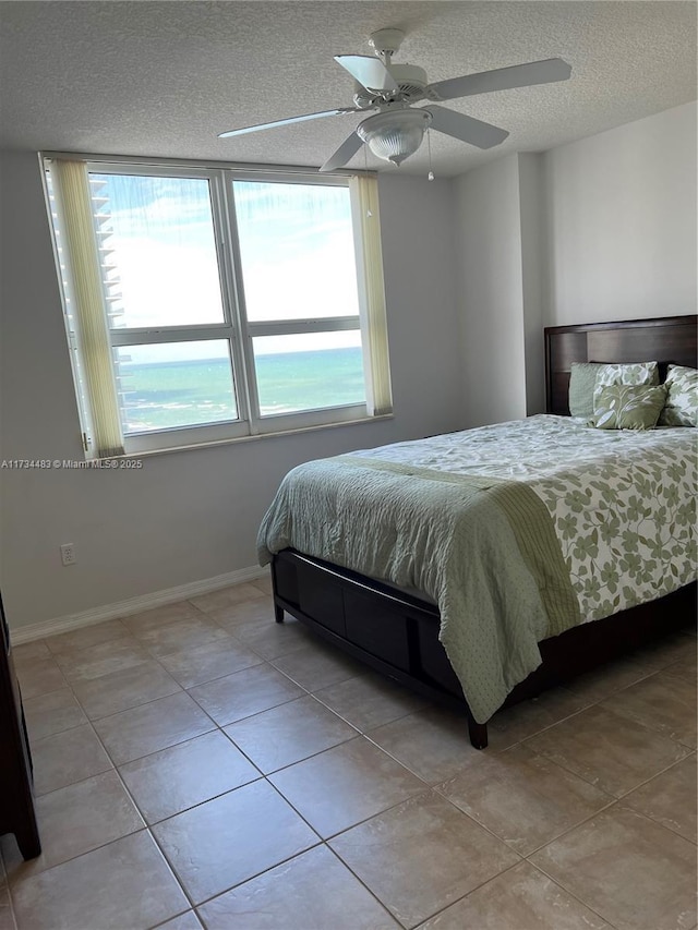 tiled bedroom featuring multiple windows, ceiling fan, a water view, and a textured ceiling